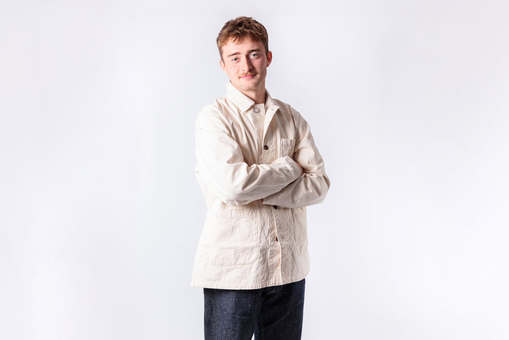 Man wearing a beige shirt and dark pants against a white background