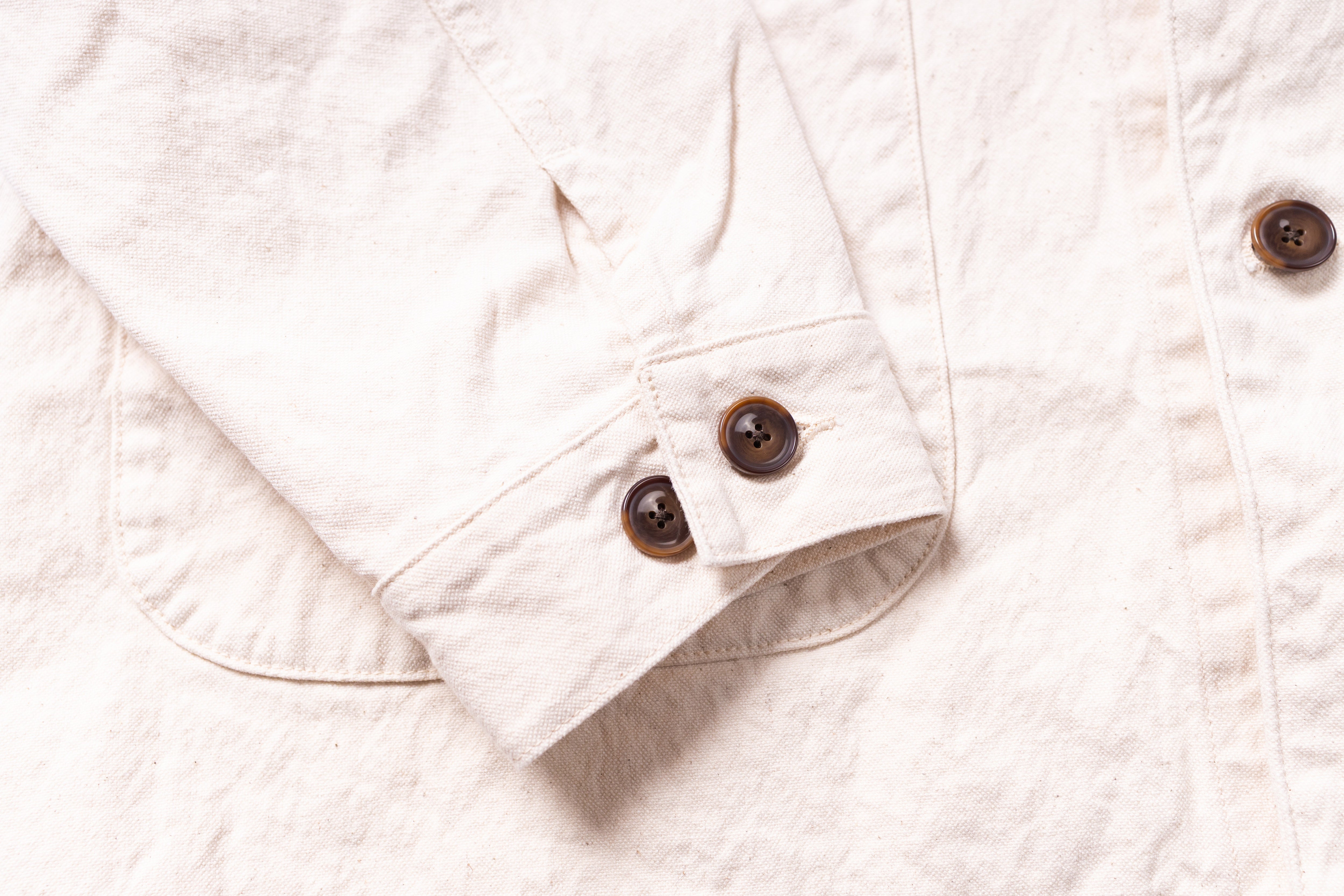 Close-up of a white quilted jacket with brown buttons on a light background