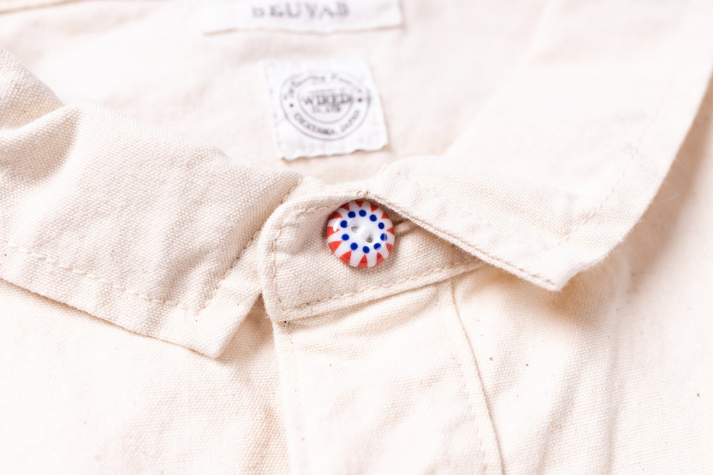 Close-up of a beige shirt with a button and a visible brand label.