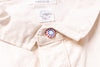 Close-up of a beige shirt with a button and a visible brand label.