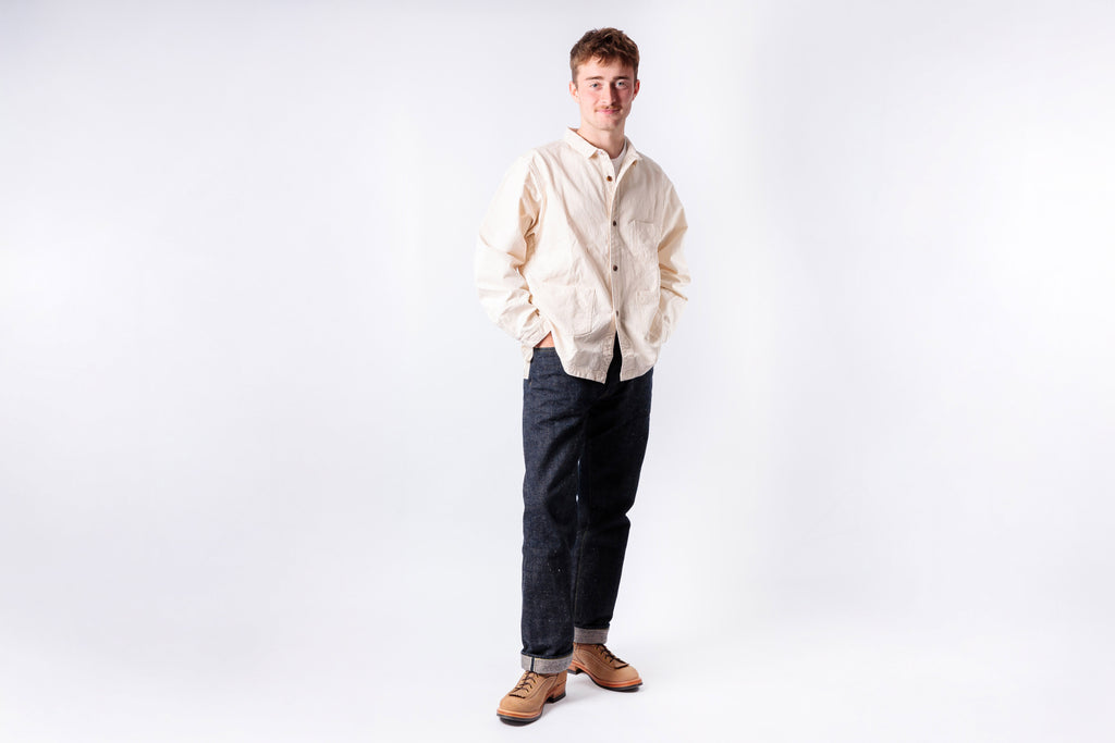 Man wearing a beige shirt and dark pants on a white background