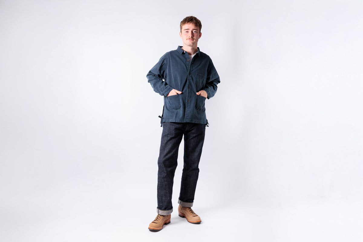 Man wearing a blue jacket and dark pants on a white background
