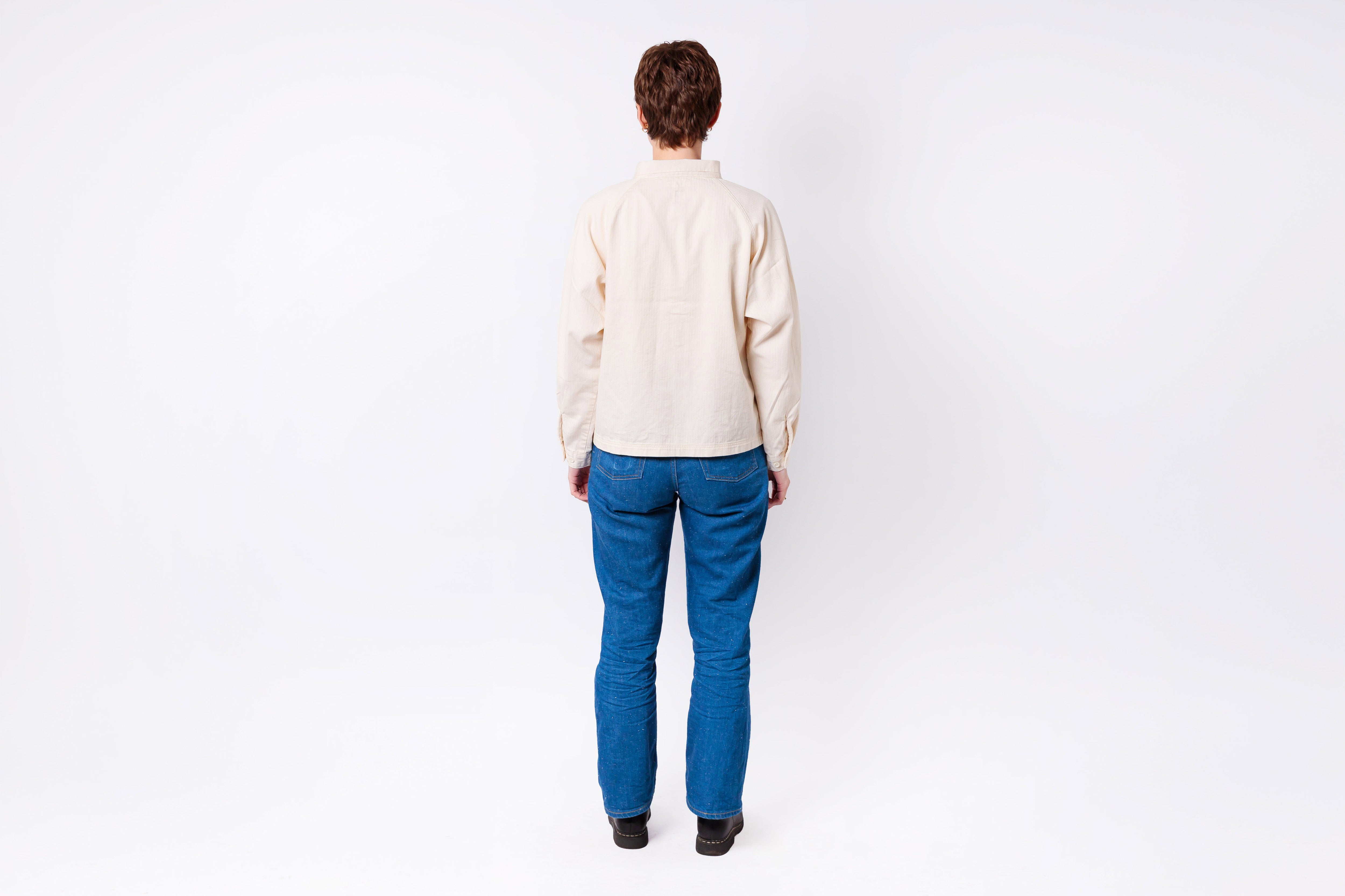 Person wearing a cream shirt and blue pants on a white background