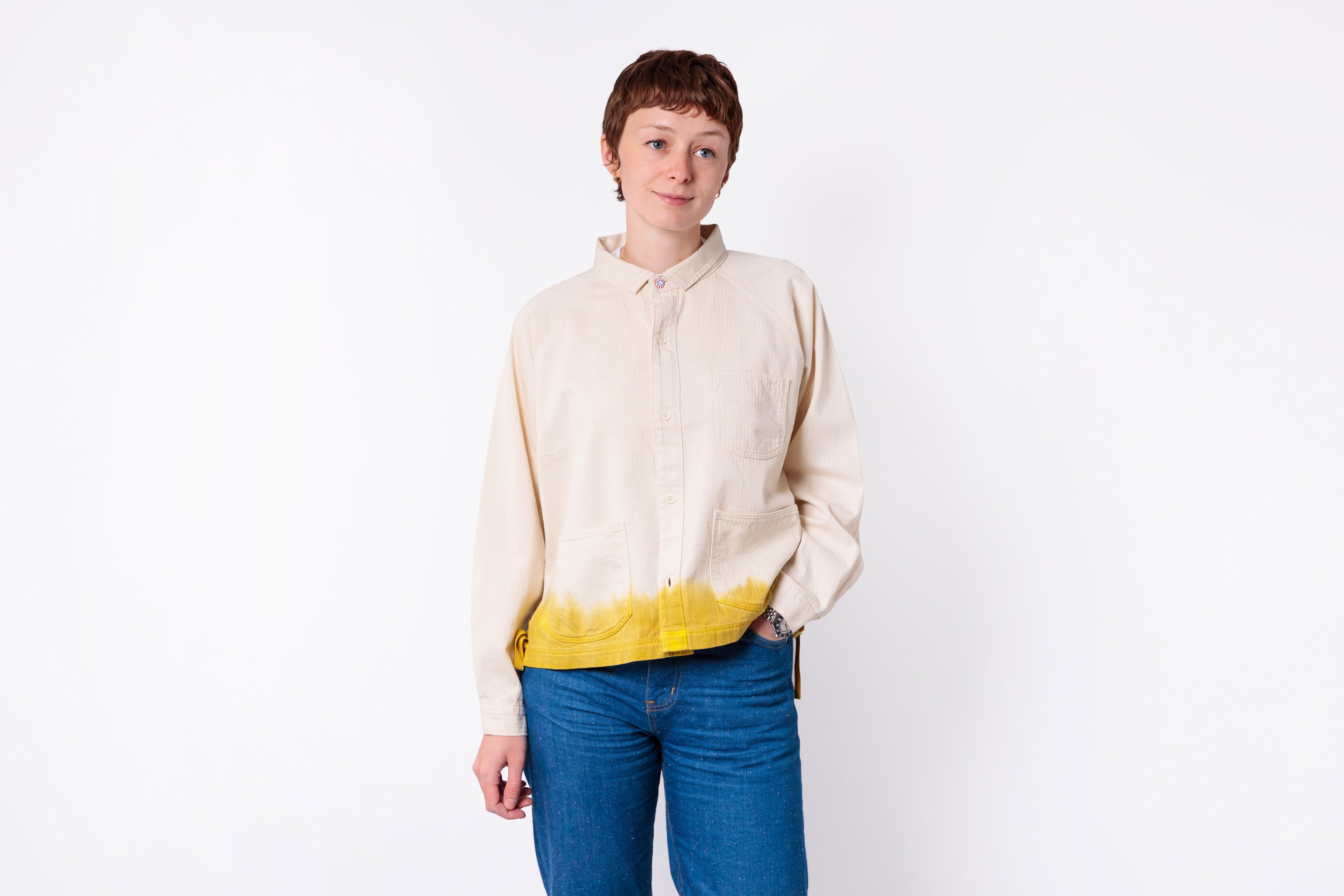 Person wearing a cream shirt with a yellow hem and blue jeans on a white background