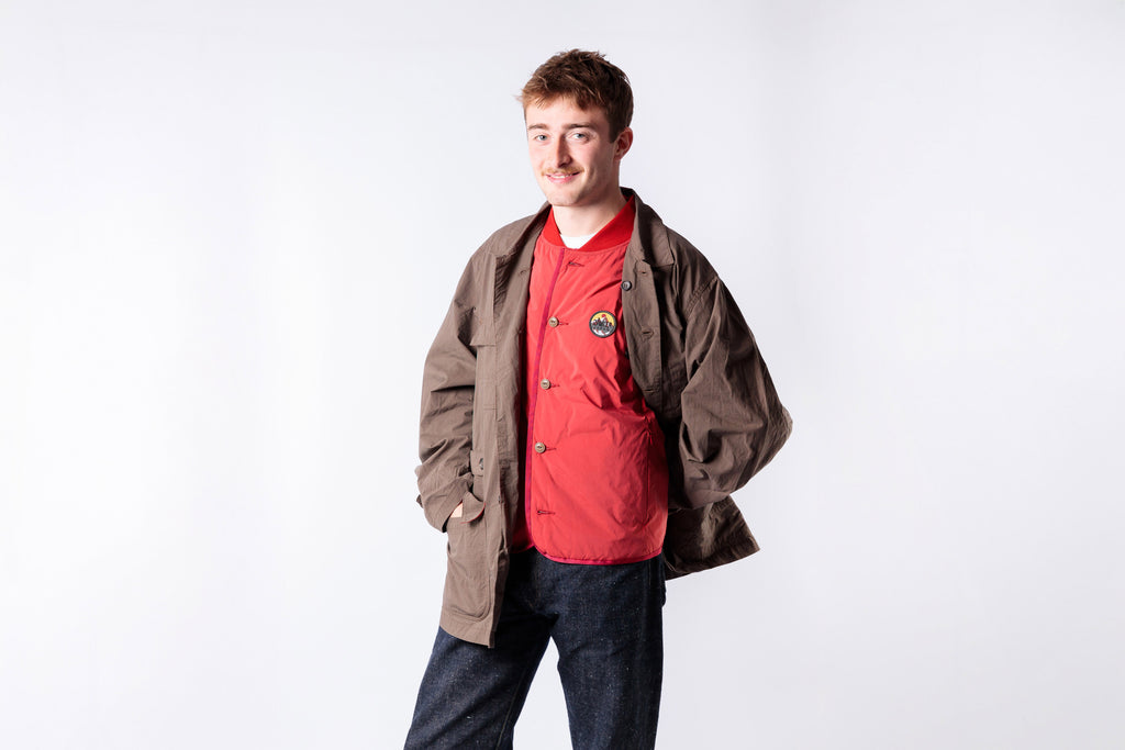 Man wearing a red shirt and brown jacket on a white background