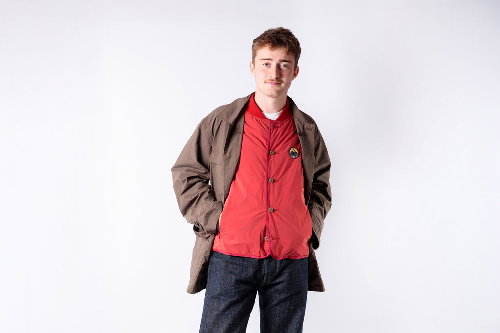 Person wearing a brown coat over a red shirt on a white background