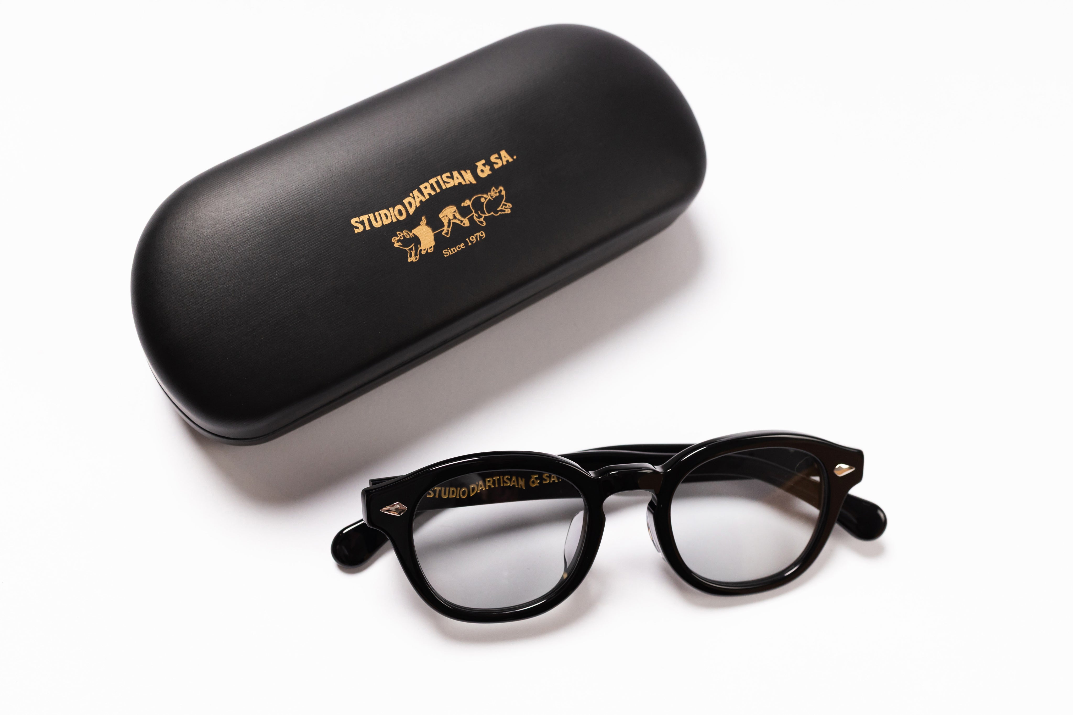 Black eyeglasses with gold text on a white background, accompanied by a matching black case.