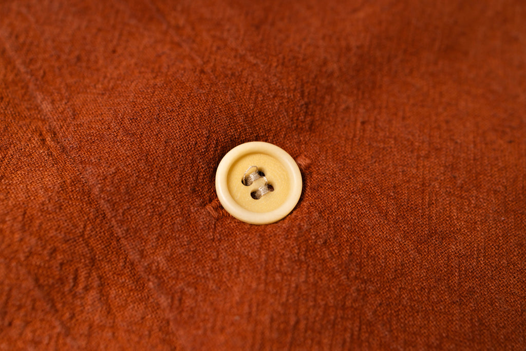 A close-up of a rust-brown textured fabric with a single cream-colored four-hole button centered on it.
