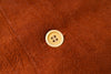 A close-up of a rust-brown textured fabric with a single cream-colored four-hole button centered on it.