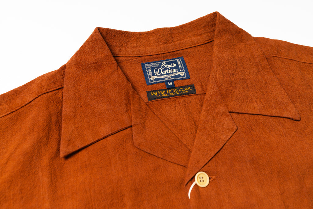 Close-up of a rust-orange suede or nubuck button-up shirt collar with a visible 'Studio D'Artisan' brand label.
