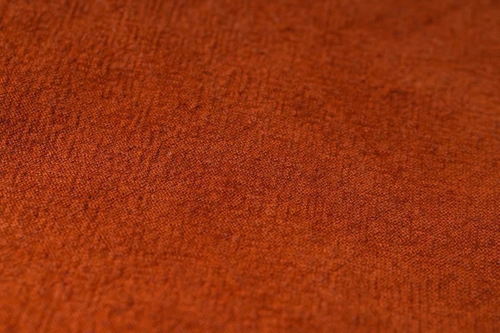 A close-up texture shot of a rust-orange woven fabric, showing the detailed knit pattern and color.