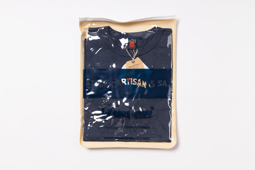 Navy blue t-shirt with 'Artisan' branding in a clear plastic bag on a white background