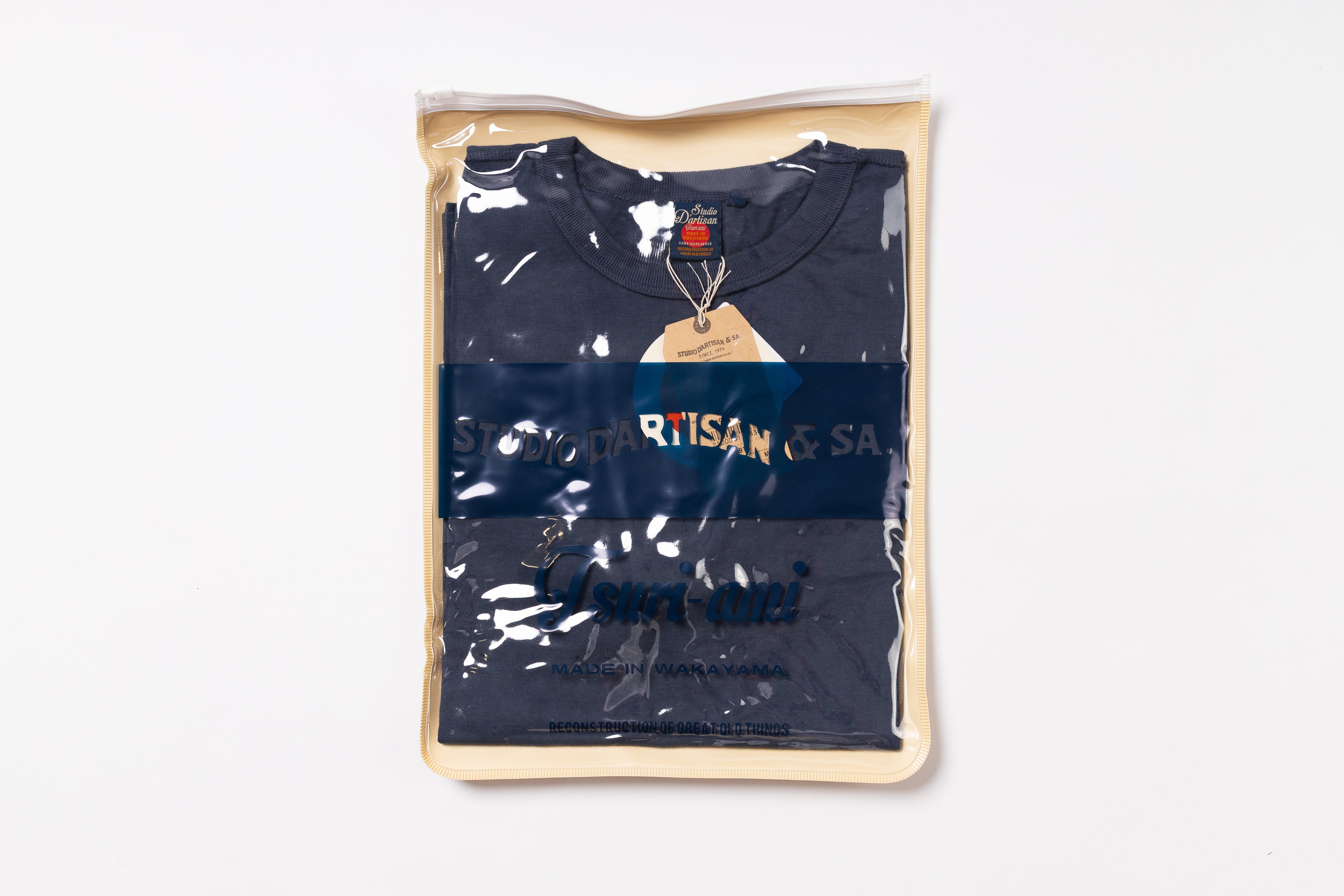 Navy blue t-shirt with 'Artisan' branding in a clear plastic bag on a white background