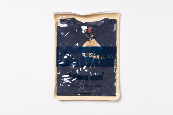 Navy blue t-shirt with 'Artisan' branding in a clear plastic bag on a white background