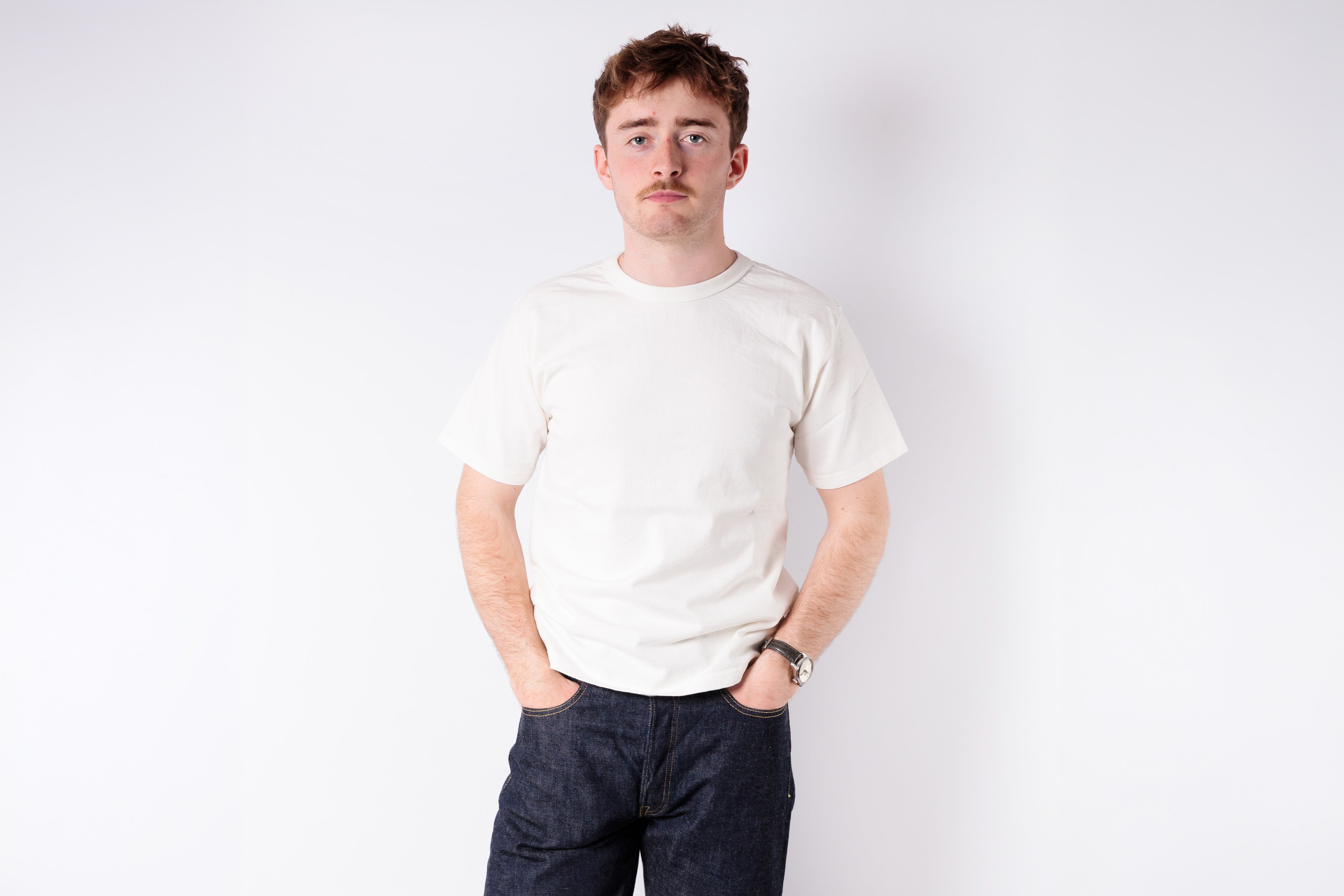 Man wearing a white t-shirt and dark pants against a plain background