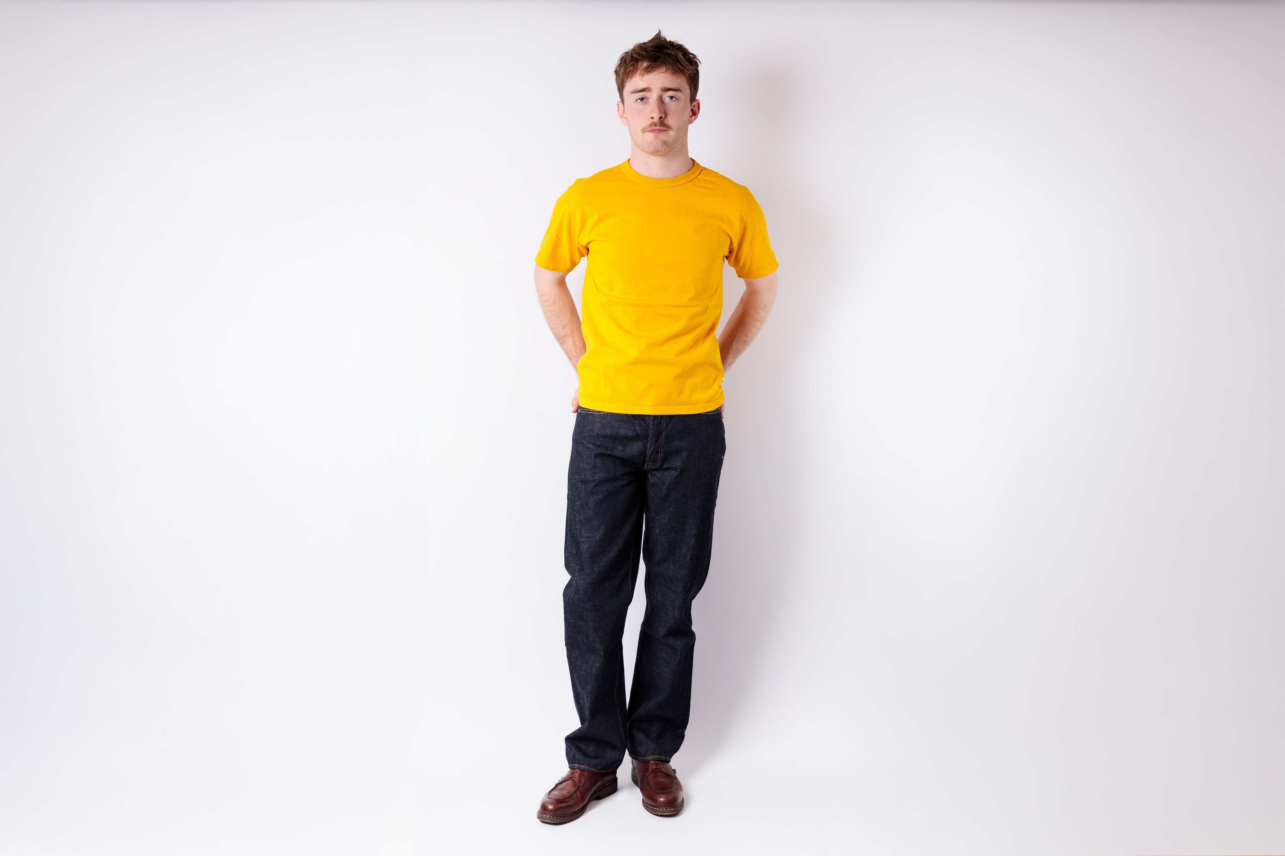 Person wearing a yellow shirt and dark pants on a white background