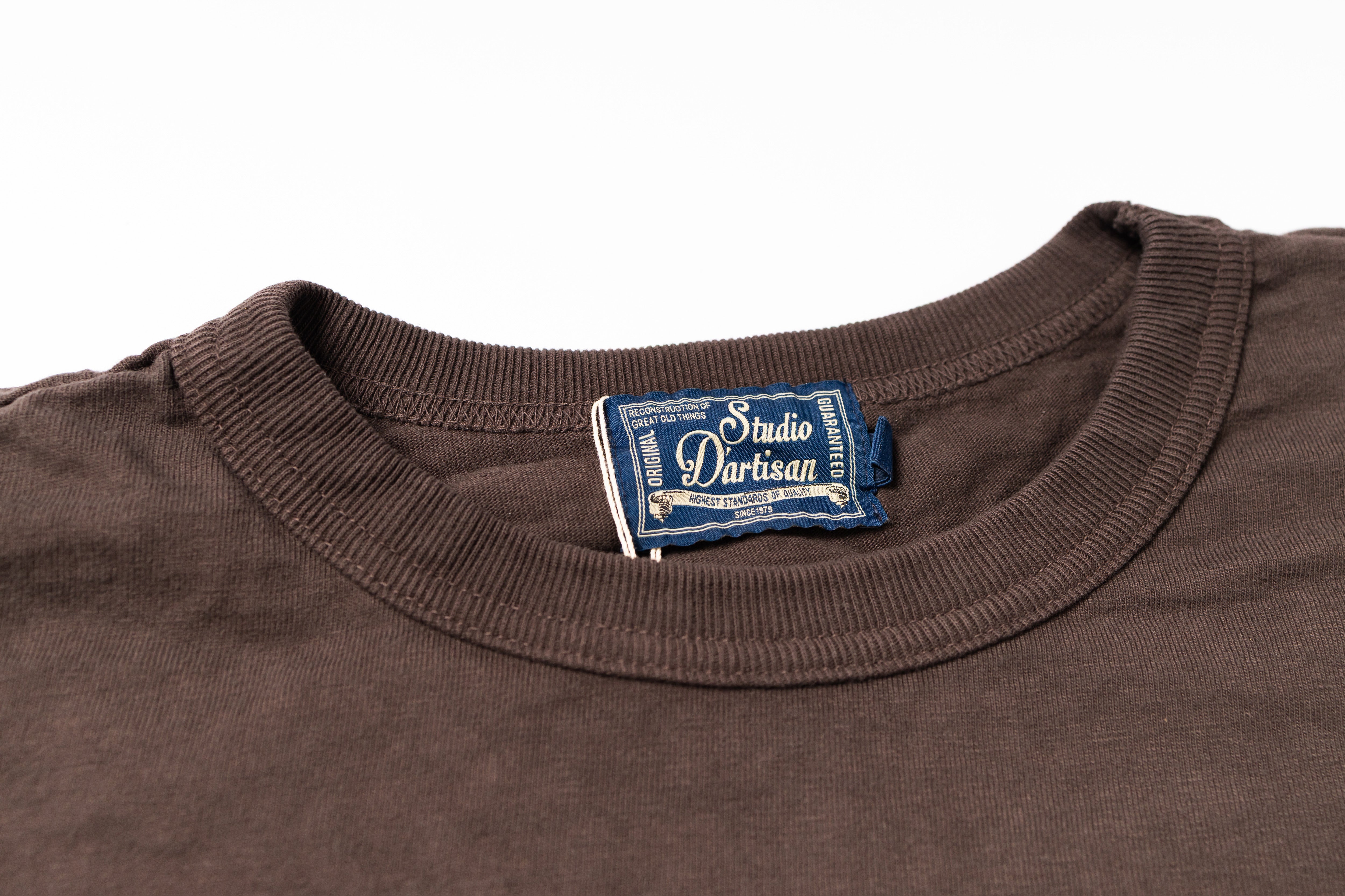 Close-up of a dark brown crewneck t-shirt showing the inner neck label which reads 'Studio D'Artisan'.