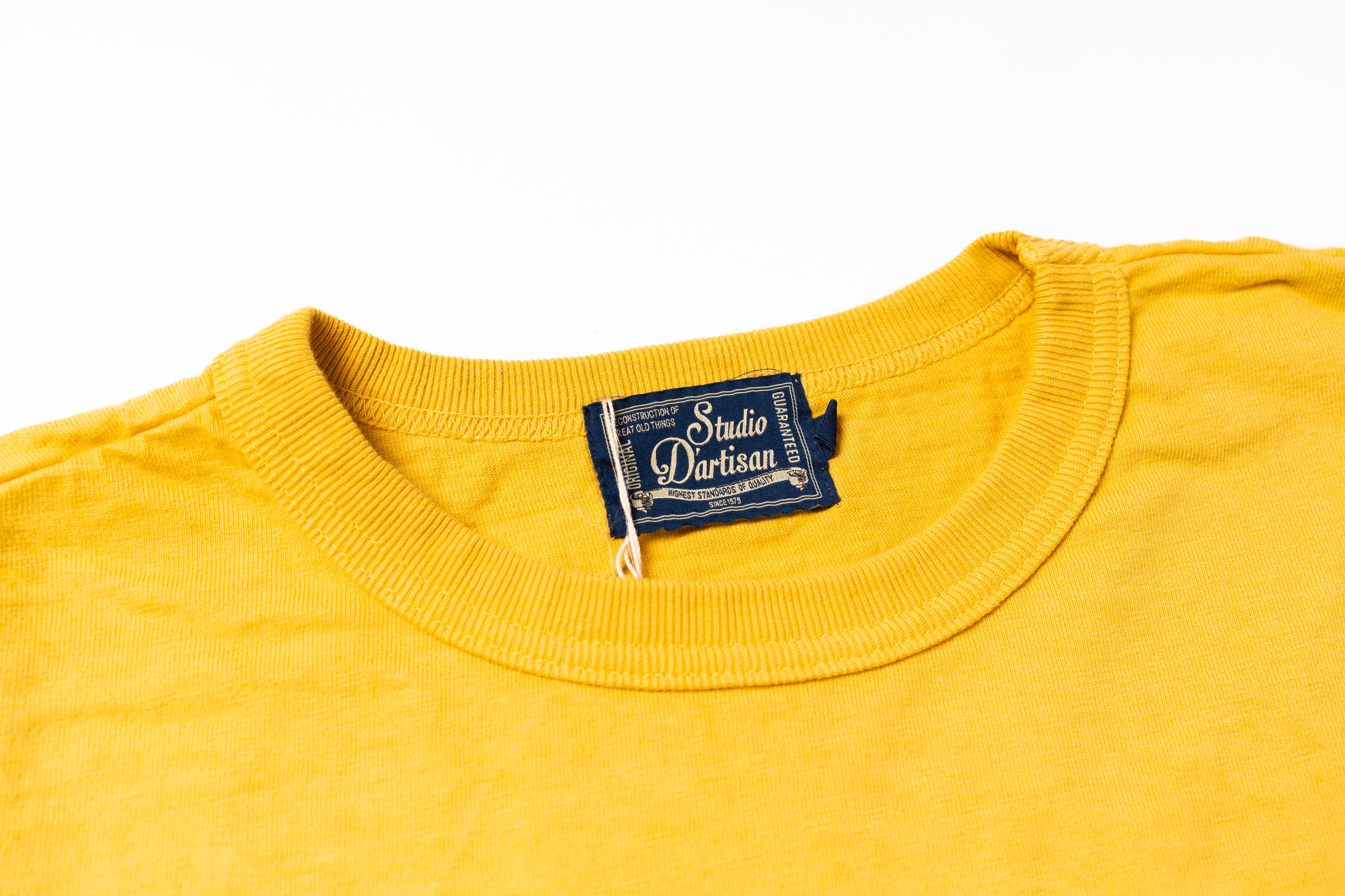 Close-up of a yellow crewneck t-shirt showing the inner neck label which reads 'Studio Dartisan'.