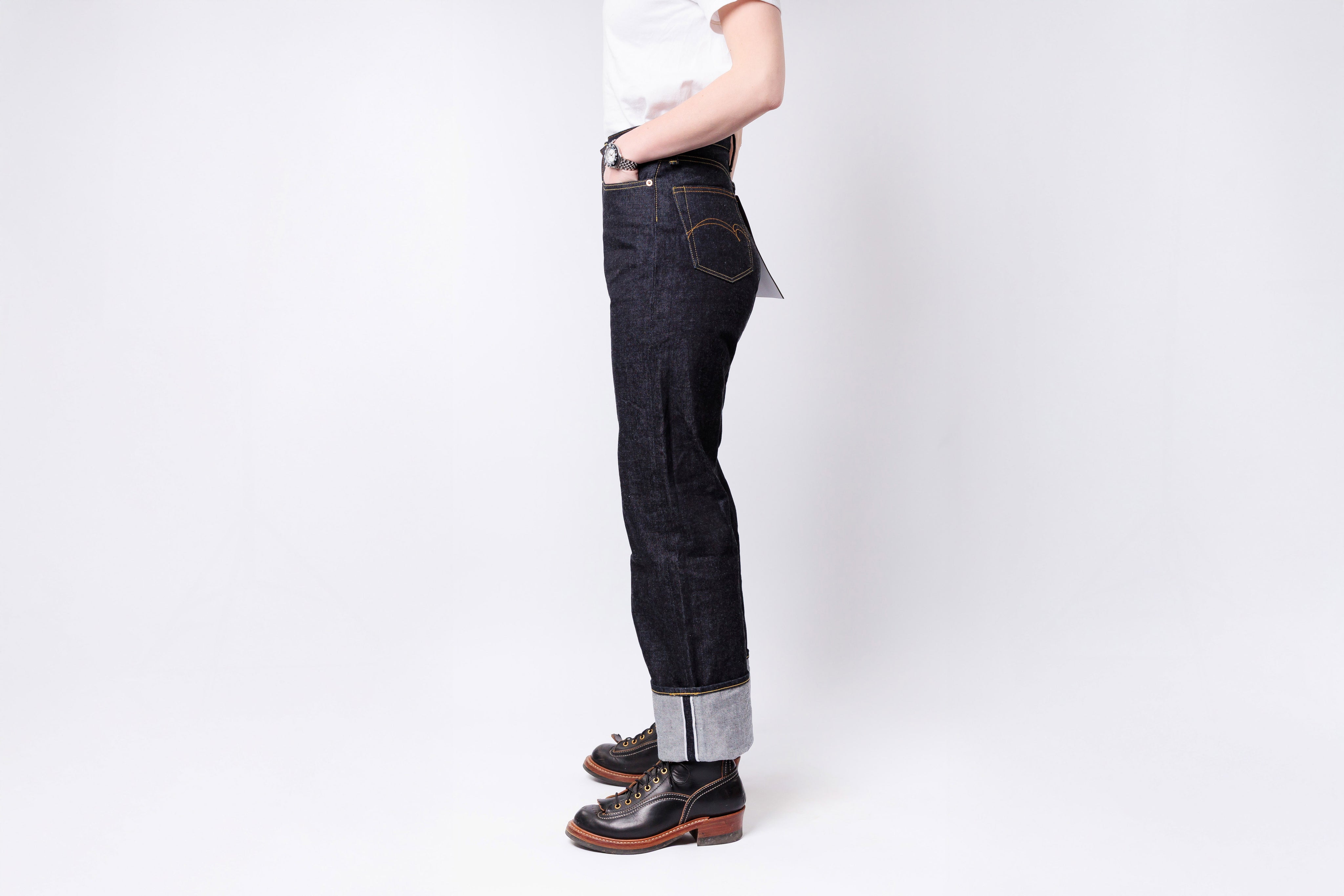 Person wearing dark jeans and brown shoes on a white background