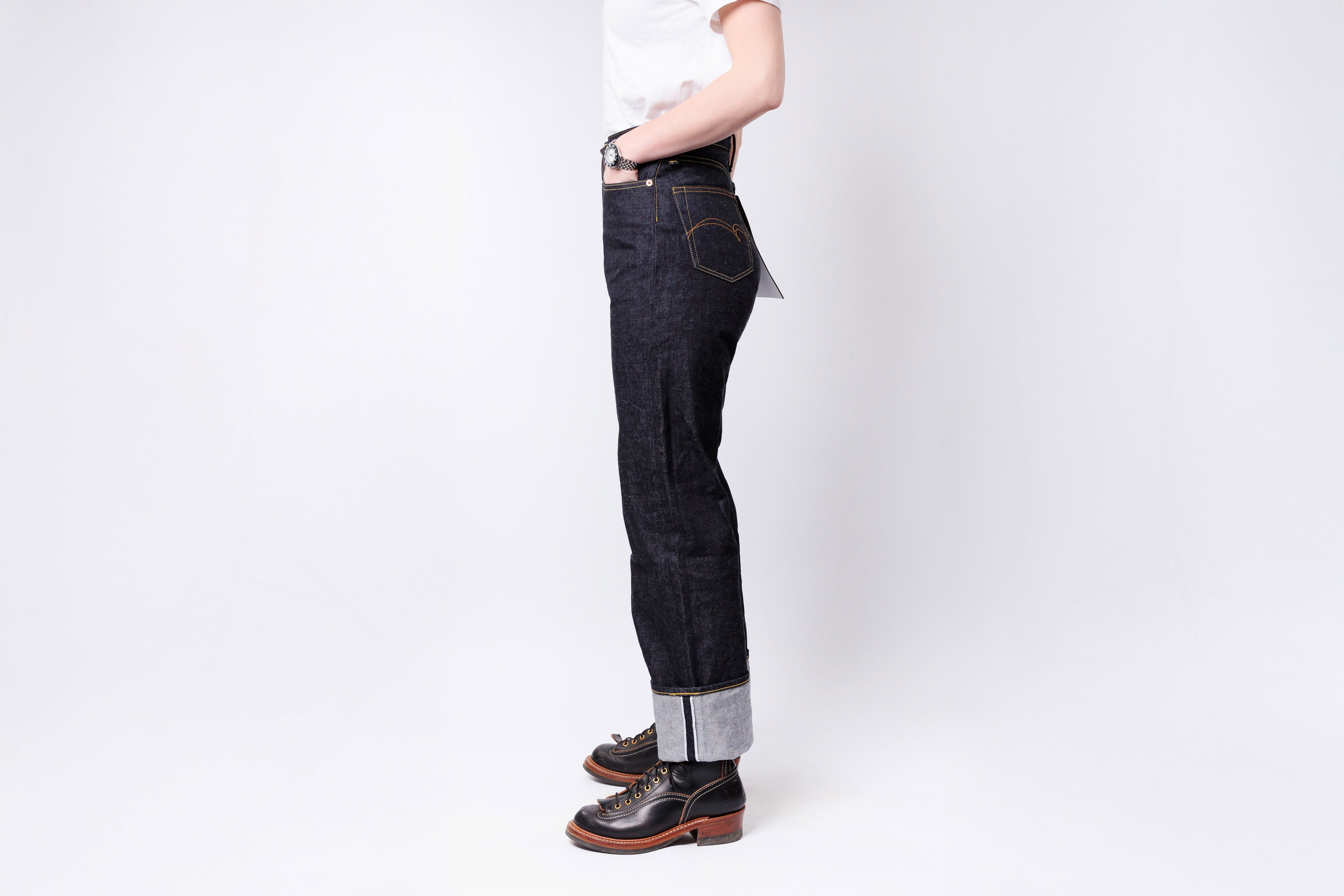 Person wearing dark jeans and brown shoes on a white background