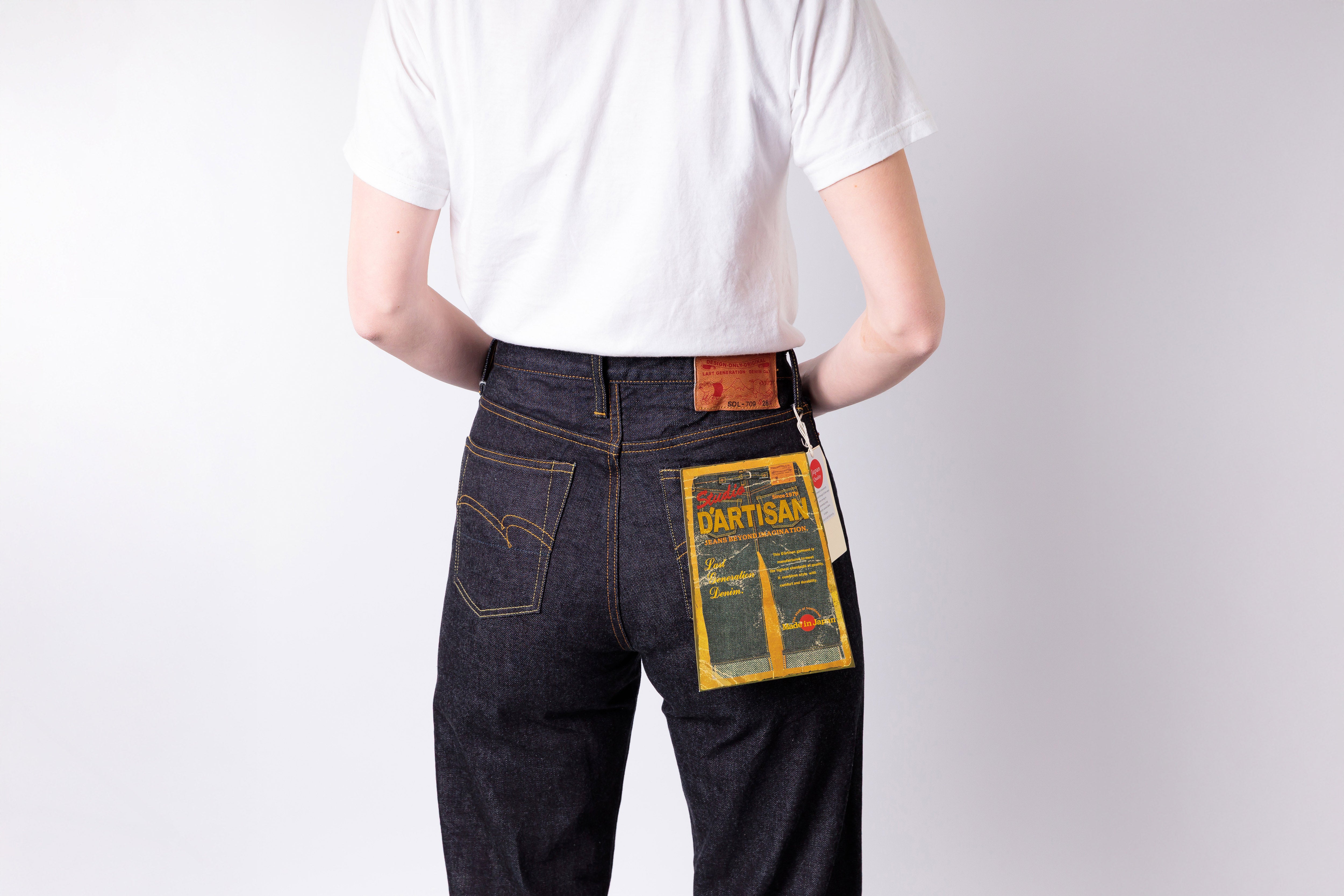 Person wearing dark blue jeans with a visible brand label on a plain background