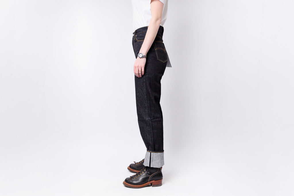 Person wearing dark jeans and brown shoes on a white background