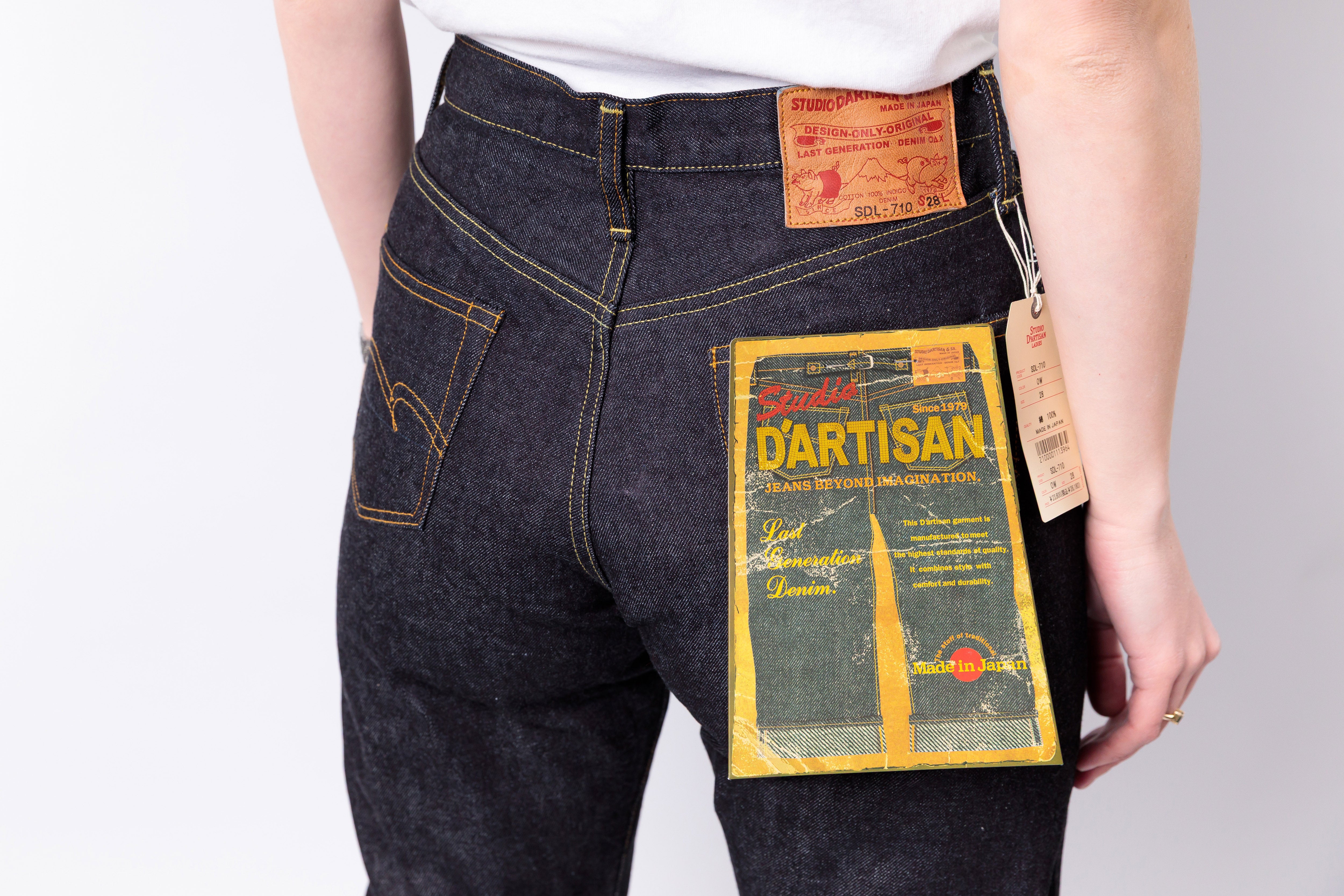 Person wearing dark blue jeans with a visible brand label on a light gray background