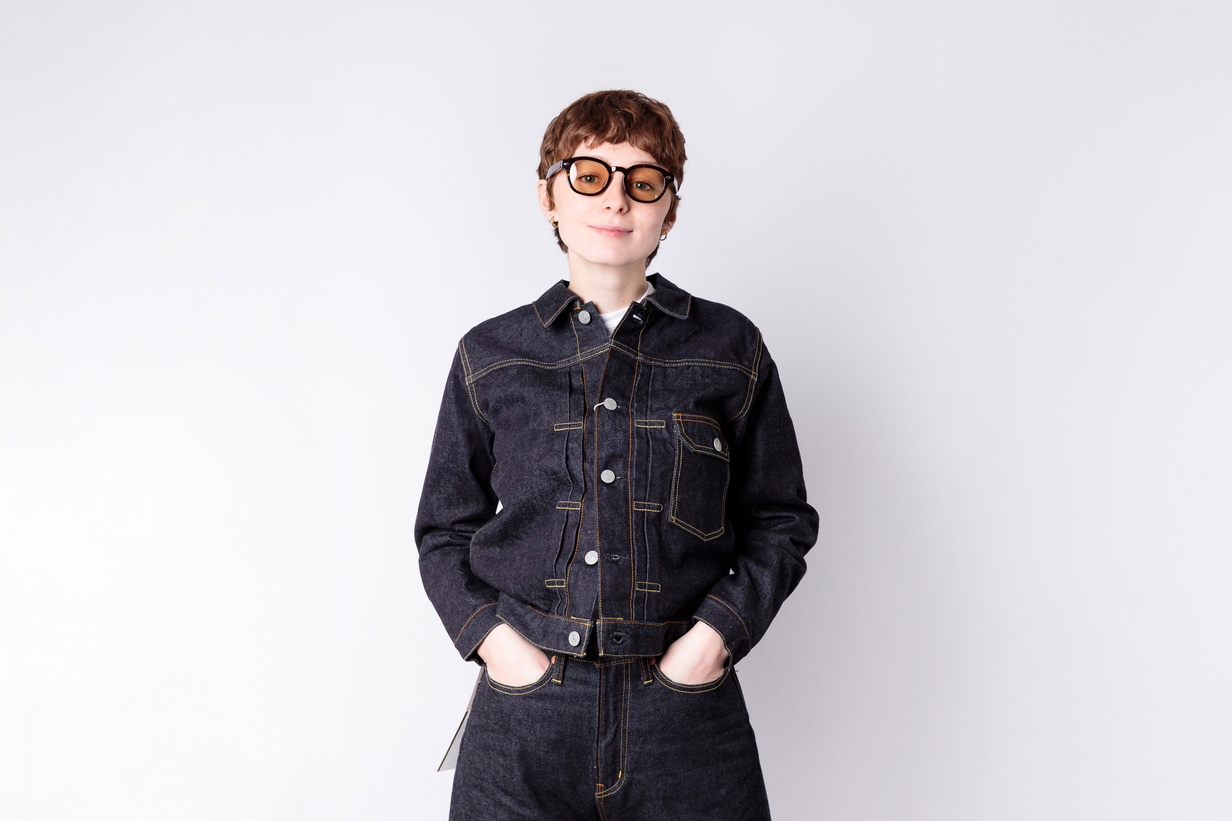 Person wearing a dark denim jacket and sunglasses on a white background