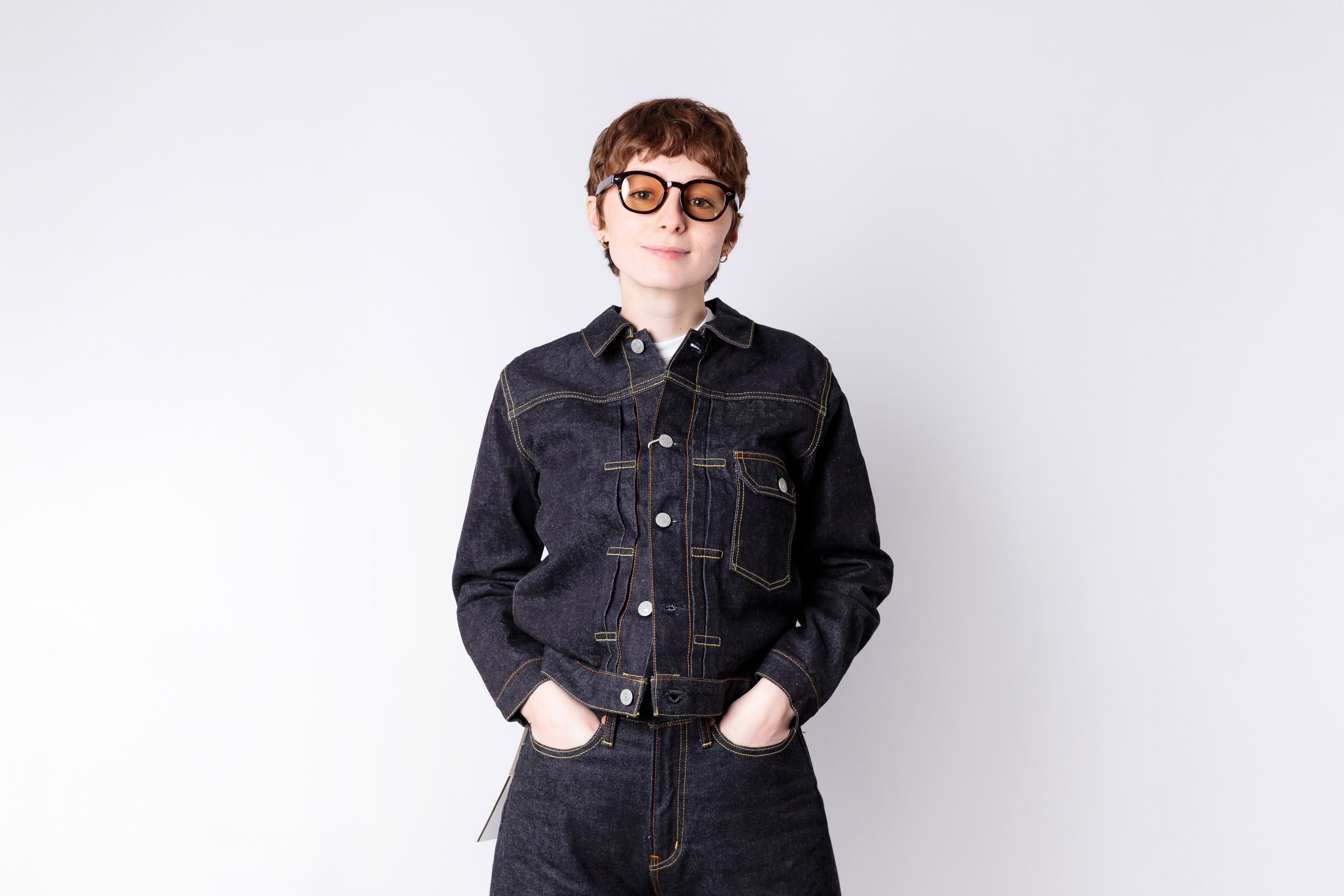 Person wearing a dark denim jacket and sunglasses on a white background