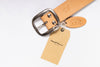 Tan leather belt with metal buckle and a tag on a white background