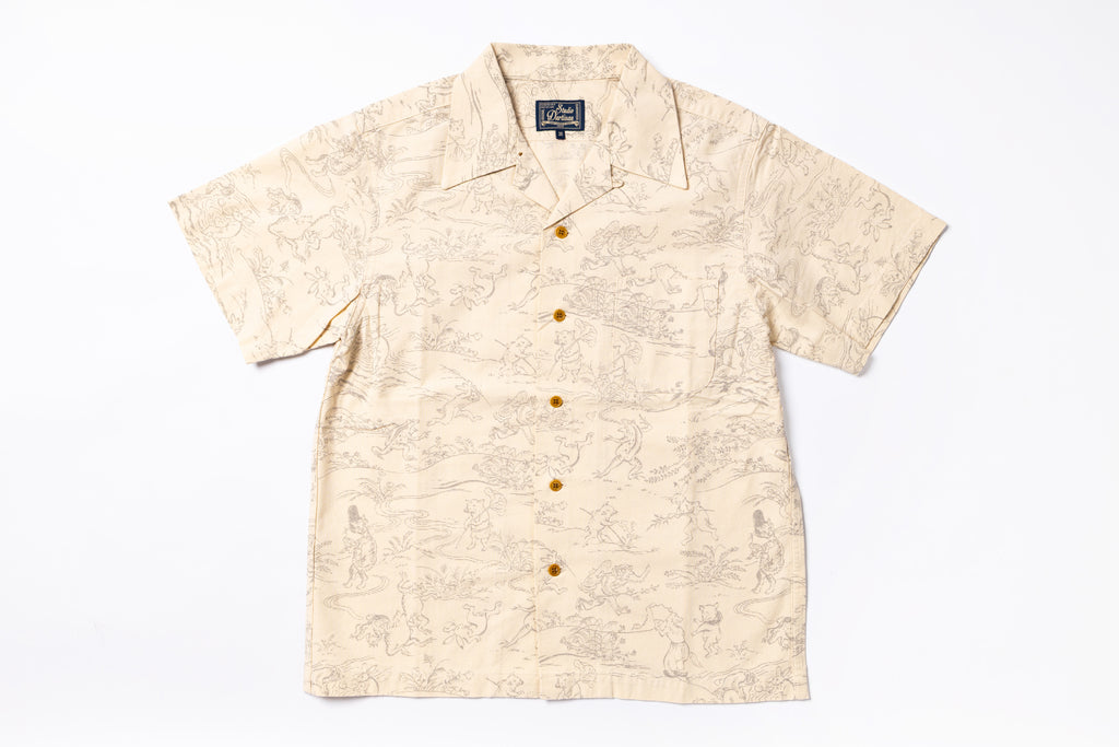 A short-sleeve camp collar button-up shirt in beige with a light brown scenic illustration pattern, featuring brown buttons down the front, laid flat on a white background.