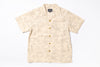 A short-sleeve camp collar button-up shirt in beige with a light brown scenic illustration pattern, featuring brown buttons down the front, laid flat on a white background.