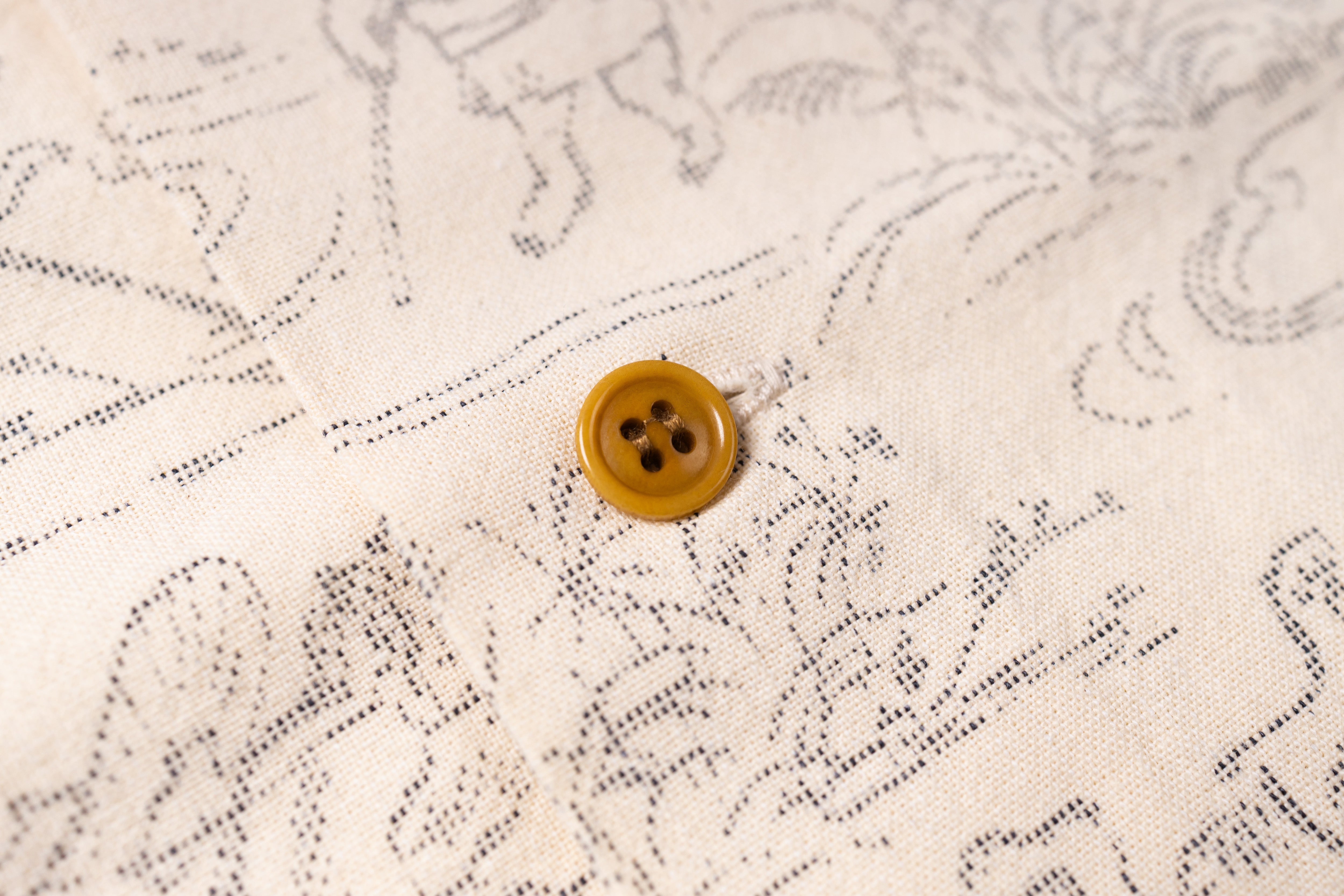 Close-up of a cream-colored fabric with a delicate black line-art pattern and a single round mustard-yellow button.