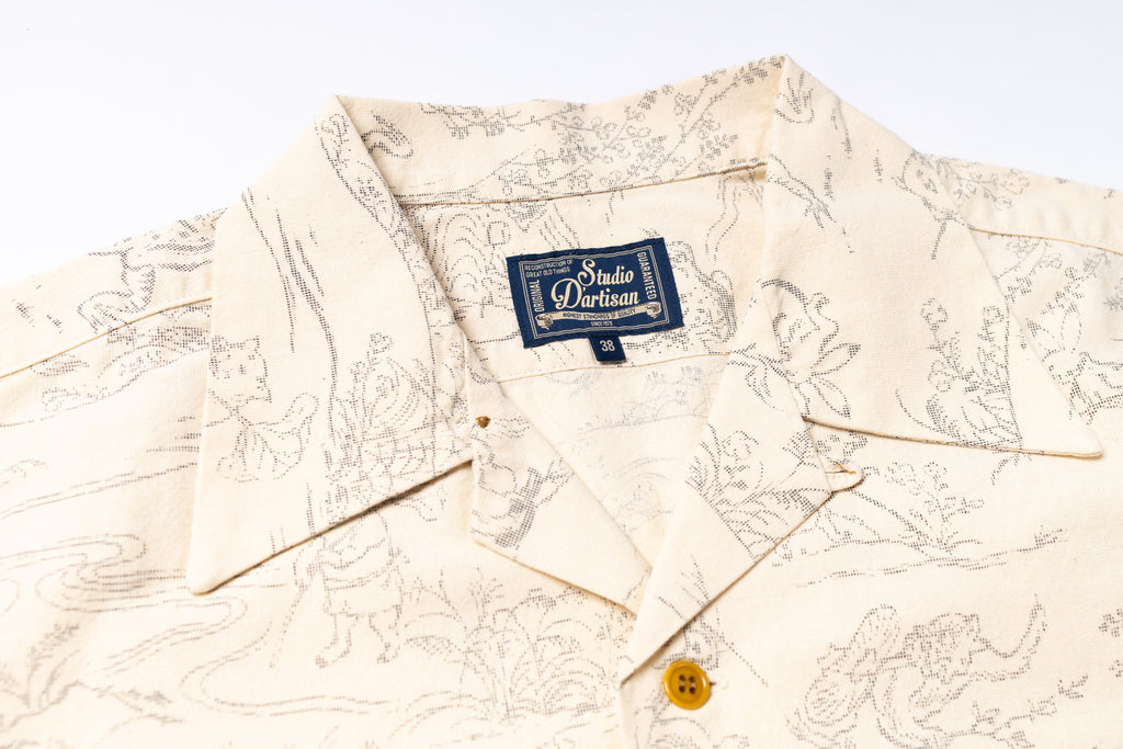 Close-up of a cream-colored short-sleeve button-up shirt with a fine gray line-art print and a visible Studio Darliau neck label.