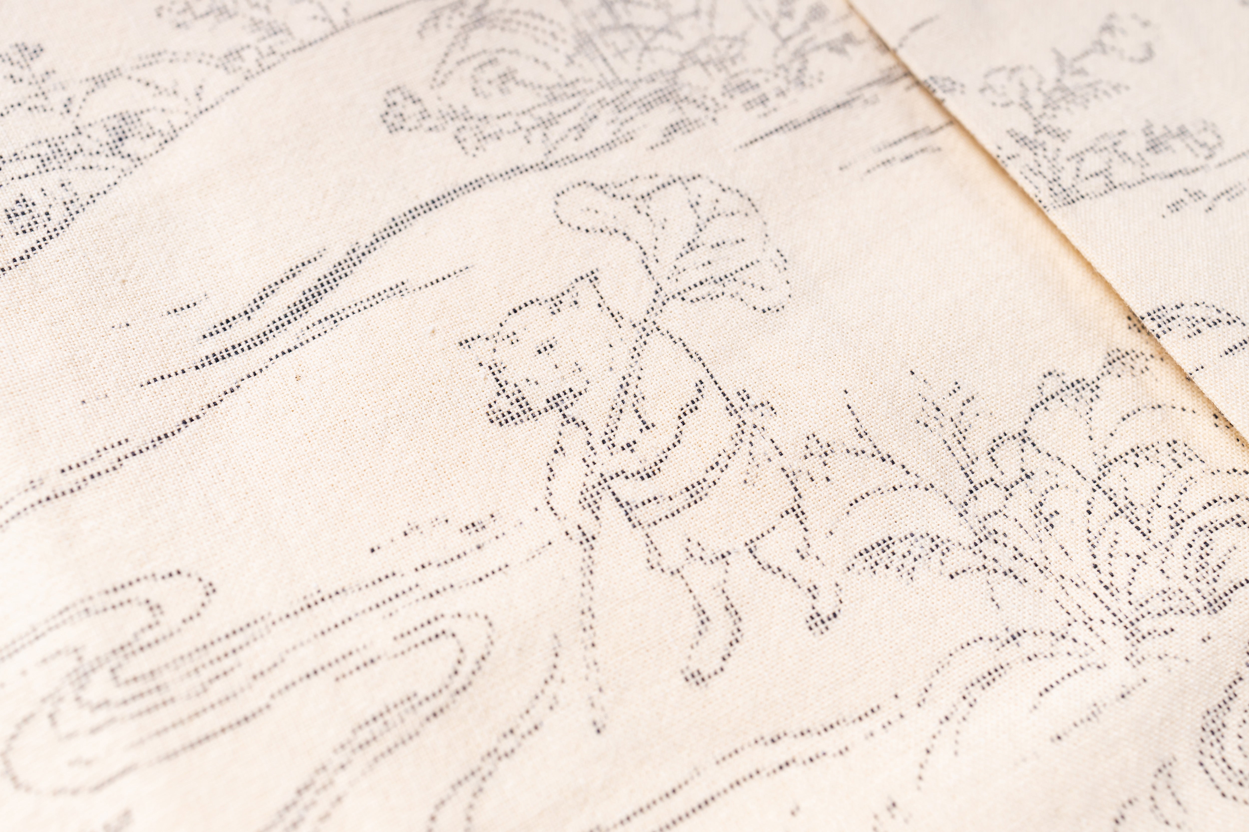Close-up of a cream-colored fabric with a fine black dotted line illustration of a figure walking among stylized plants and waves.