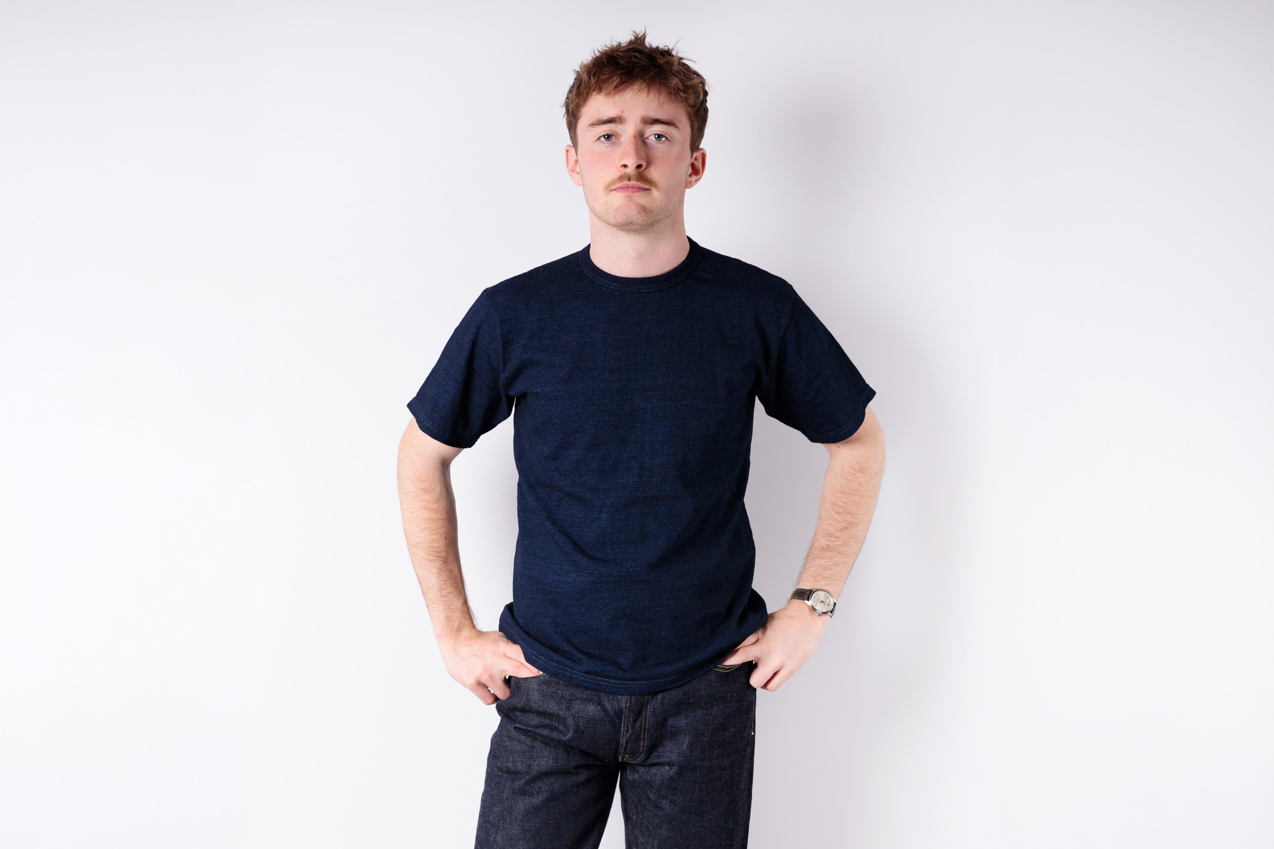 Man wearing a dark blue t-shirt and jeans against a white background