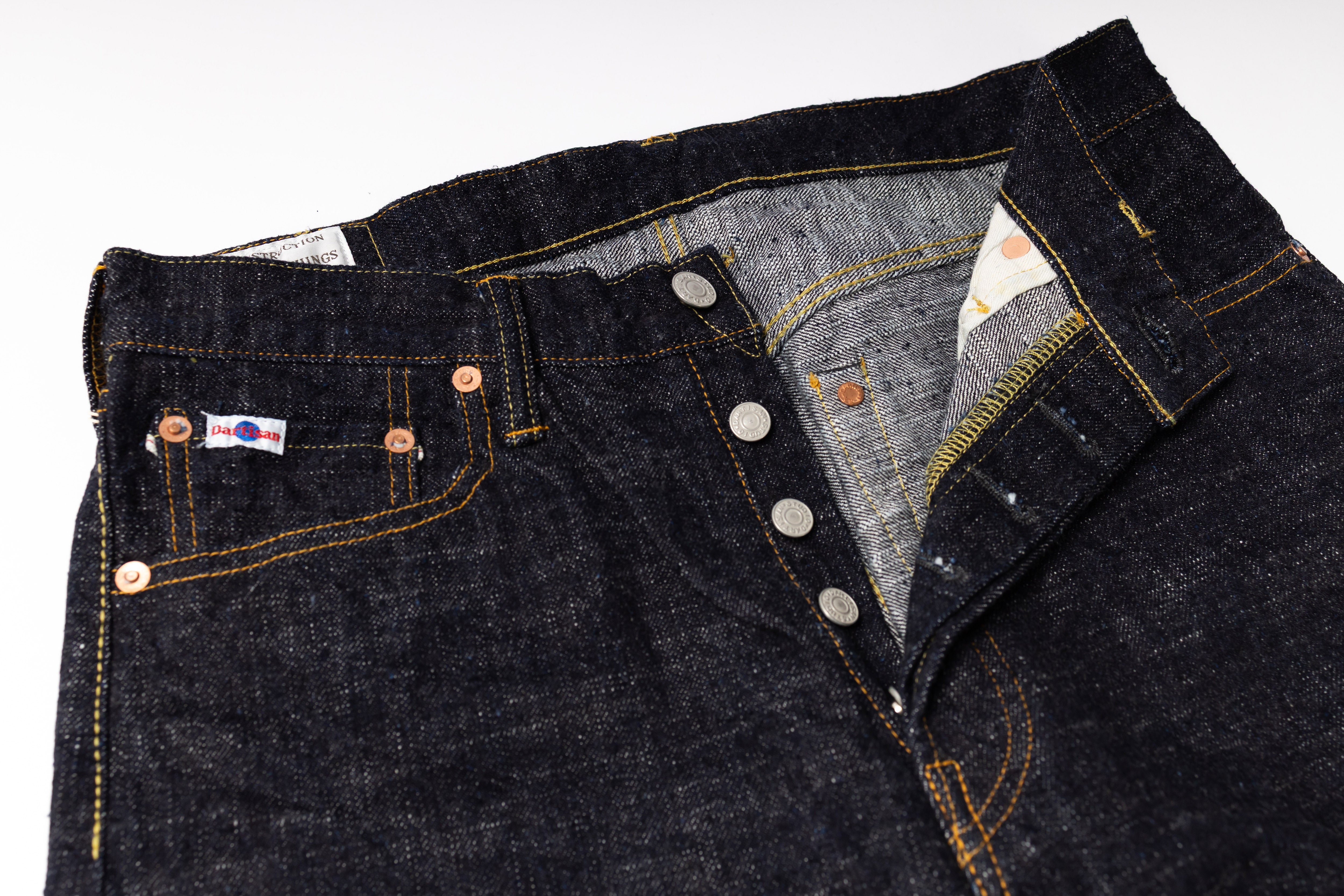 Close-up of dark blue denim jeans with visible stitching and buttons on a white background