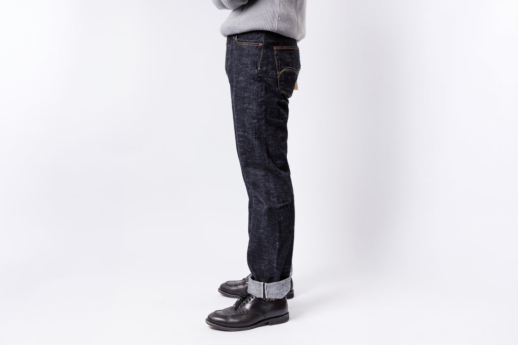 Person wearing dark blue jeans and black shoes on a white background