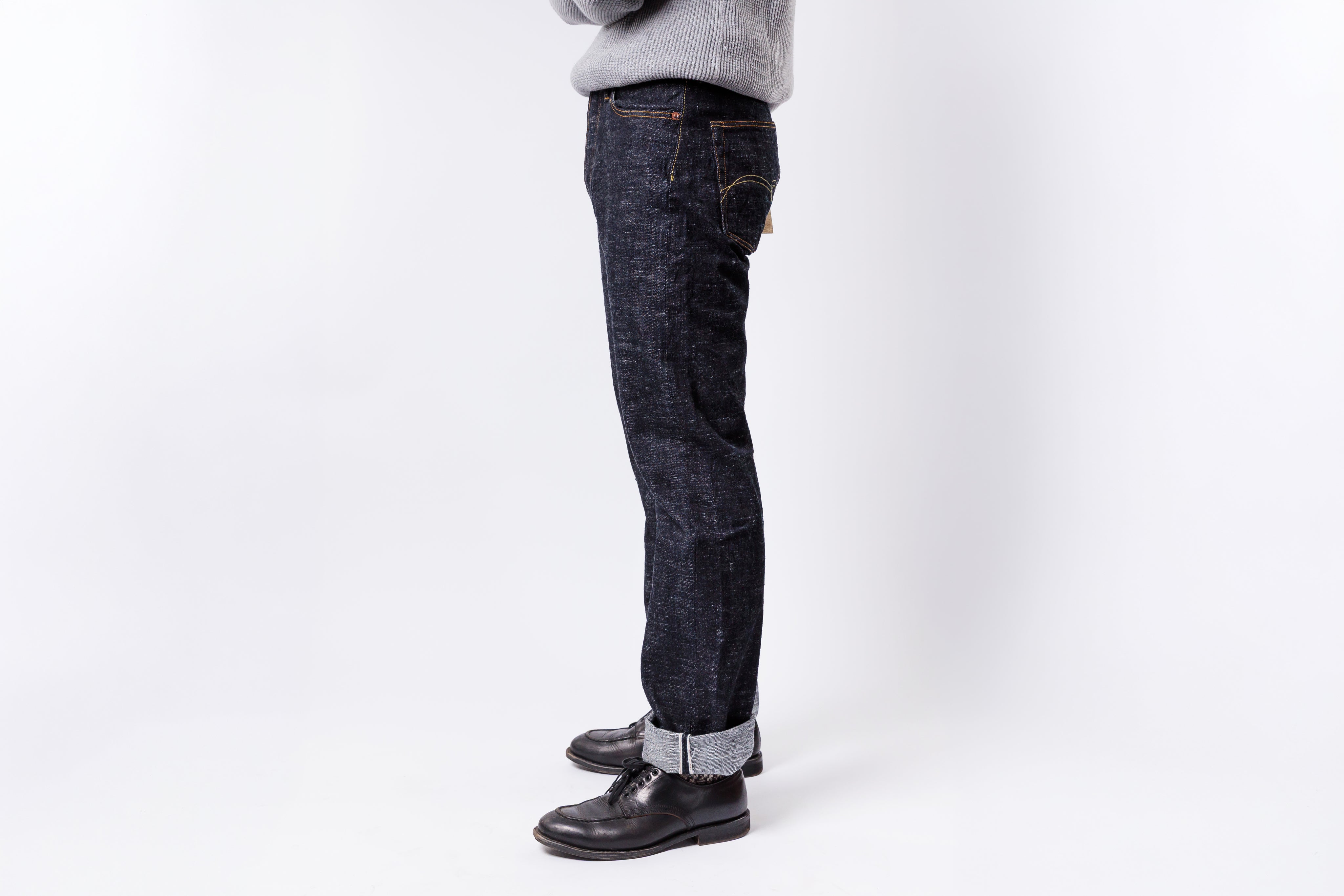 Person wearing dark blue jeans and black shoes on a white background