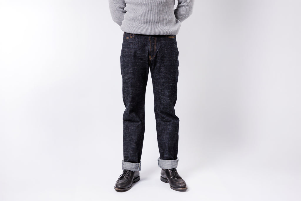 Person wearing dark jeans and a light gray sweater on a white background