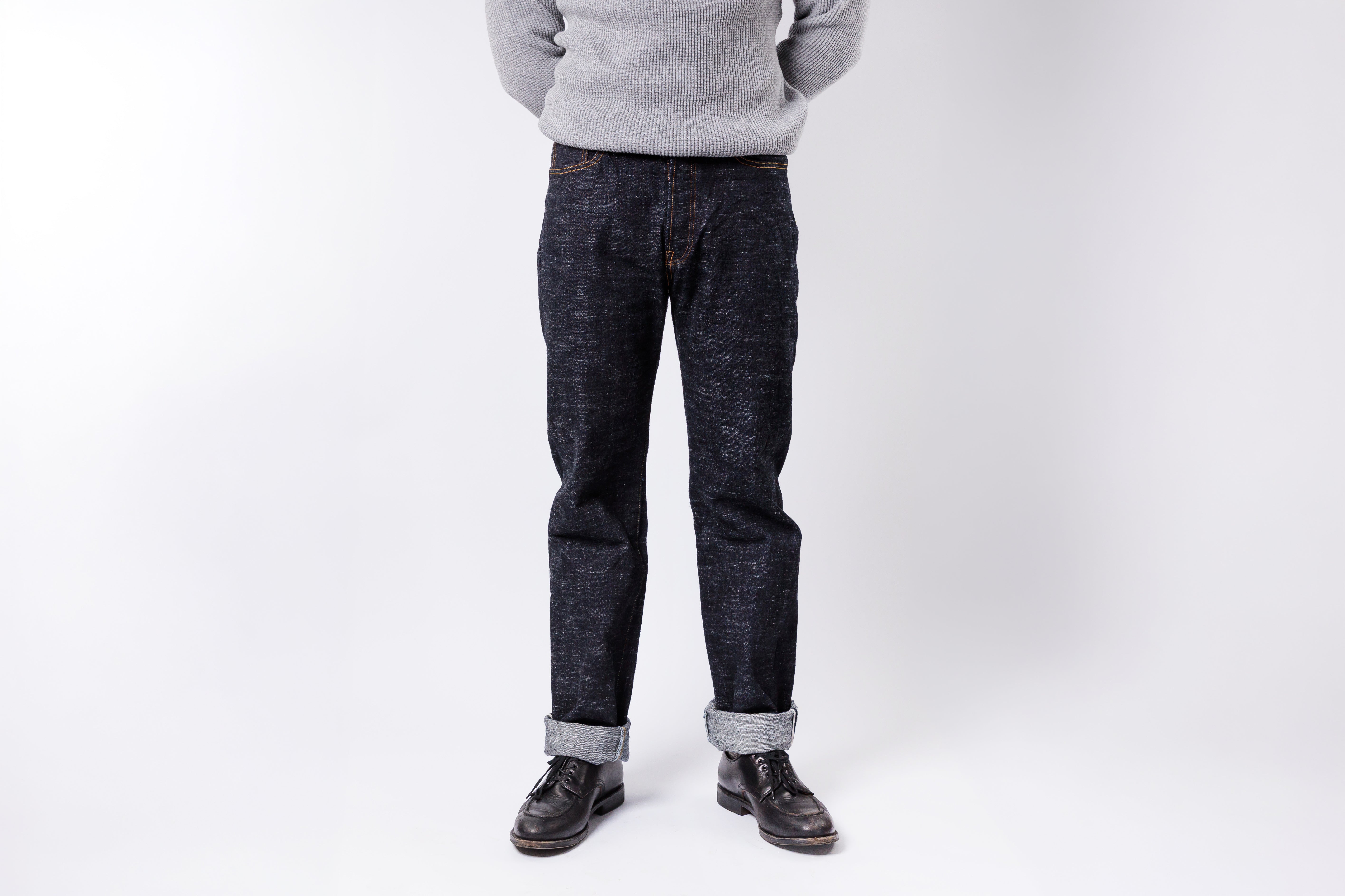 Person wearing dark jeans and a light gray sweater on a white background
