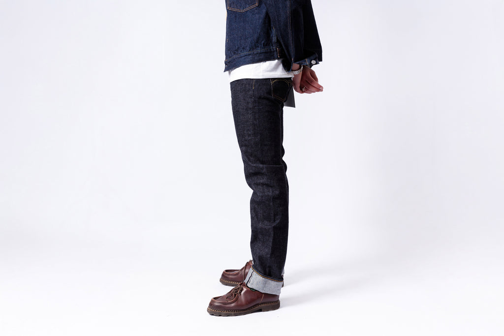 Person wearing dark jeans and brown shoes on a white background