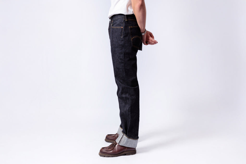 Person wearing dark blue jeans and brown shoes on a white background