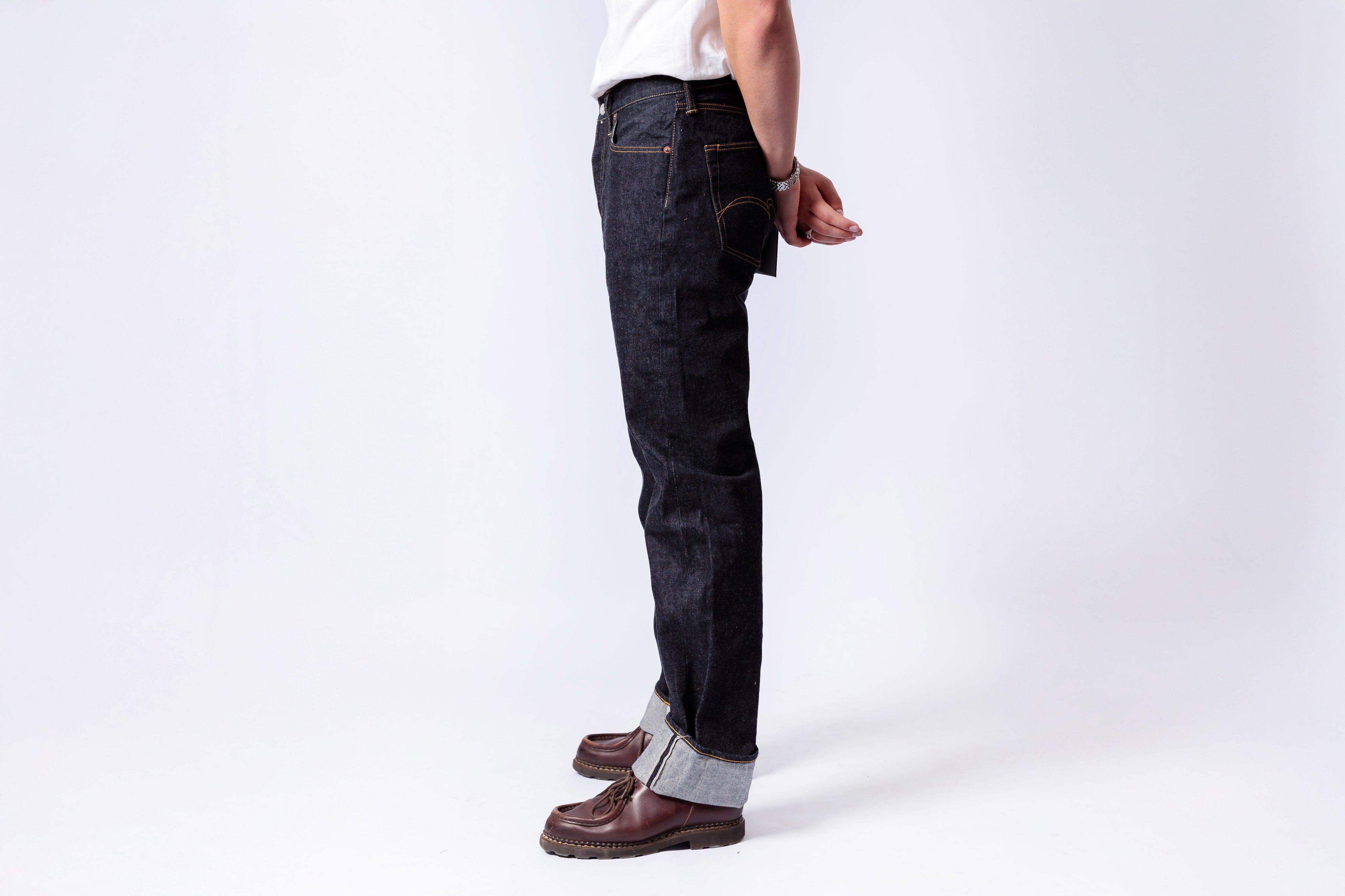 Person wearing dark blue jeans and brown shoes on a white background
