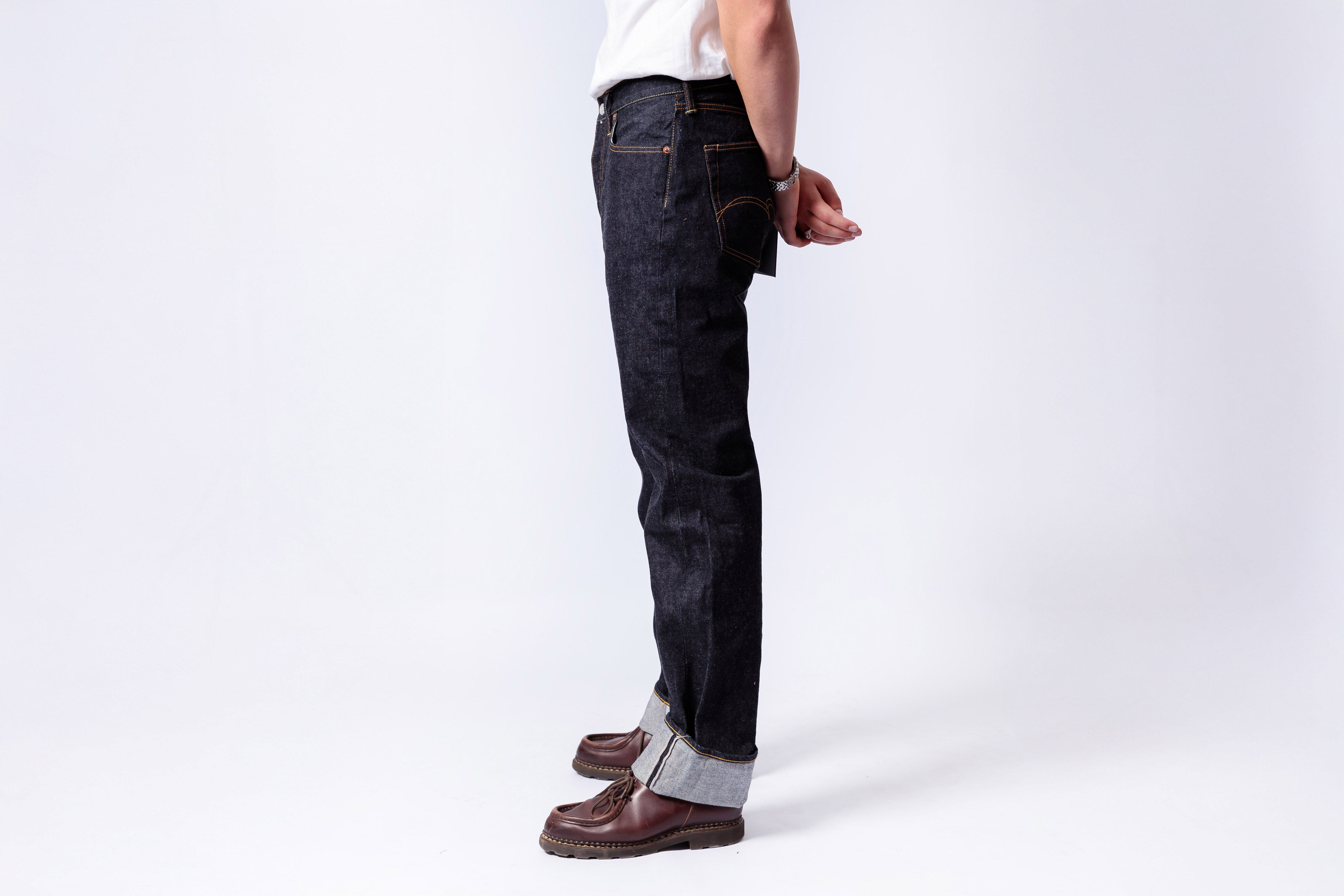 Person wearing dark blue jeans and brown shoes on a white background