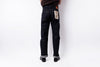 Rear view of a person wearing dark indigo denim jeans with cuffed hems and black shoes, standing against a plain white studio background.