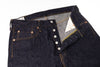 Close-up of a pair of dark indigo denim jeans with a button fly and contrast orange stitching, shown on a white background.