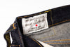Close-up of the inner waistband of dark indigo denim jeans, showing a white woven label that reads 'RECONSTRUCTION OF GREAT OLD THINGS', 'SINCE 1979', and 'STUDIO D'ARTISAN' with a small red dot, alongside yellow contrast stitching.