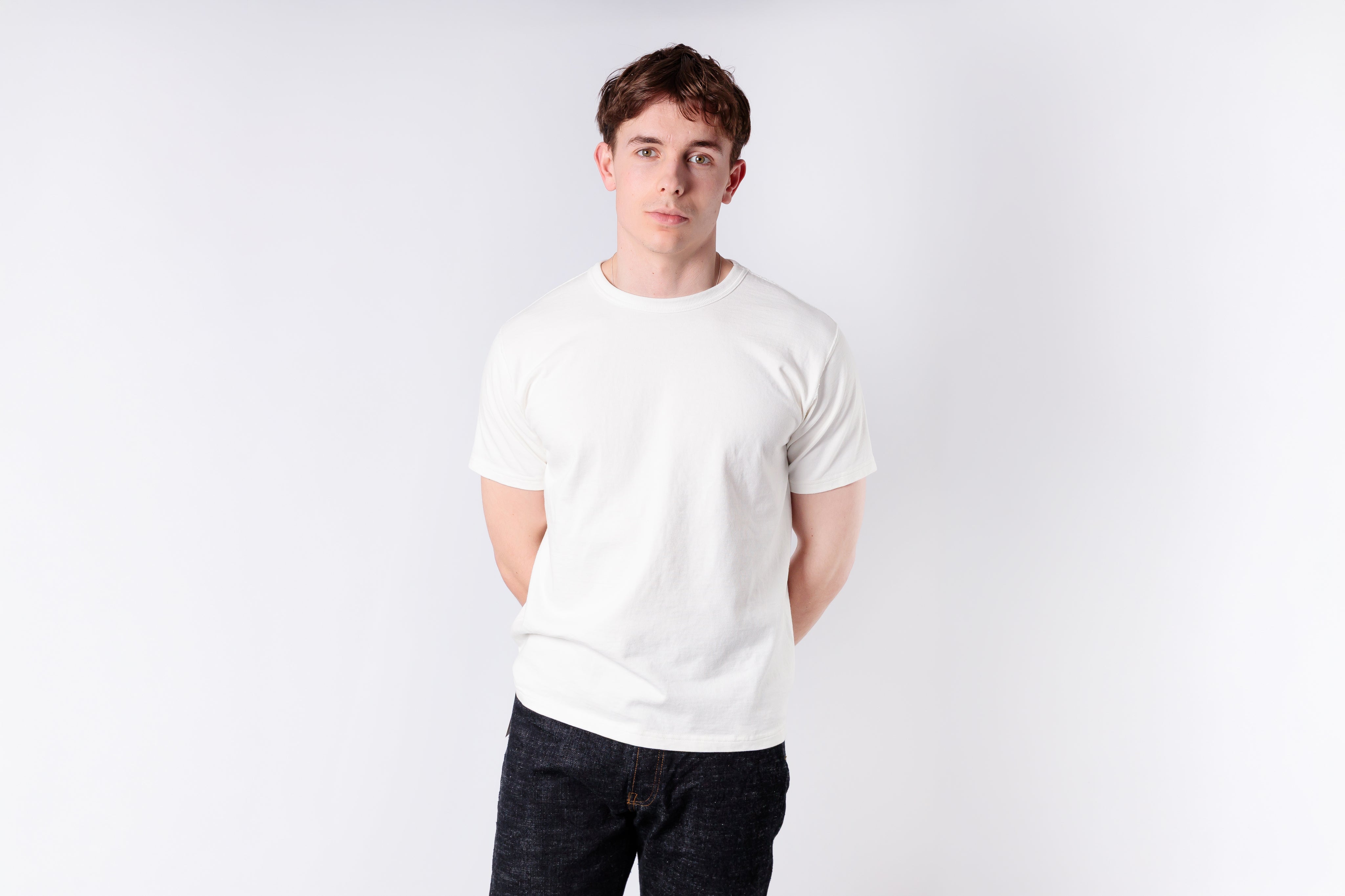 Person wearing a plain white t-shirt and dark pants on a light gray background