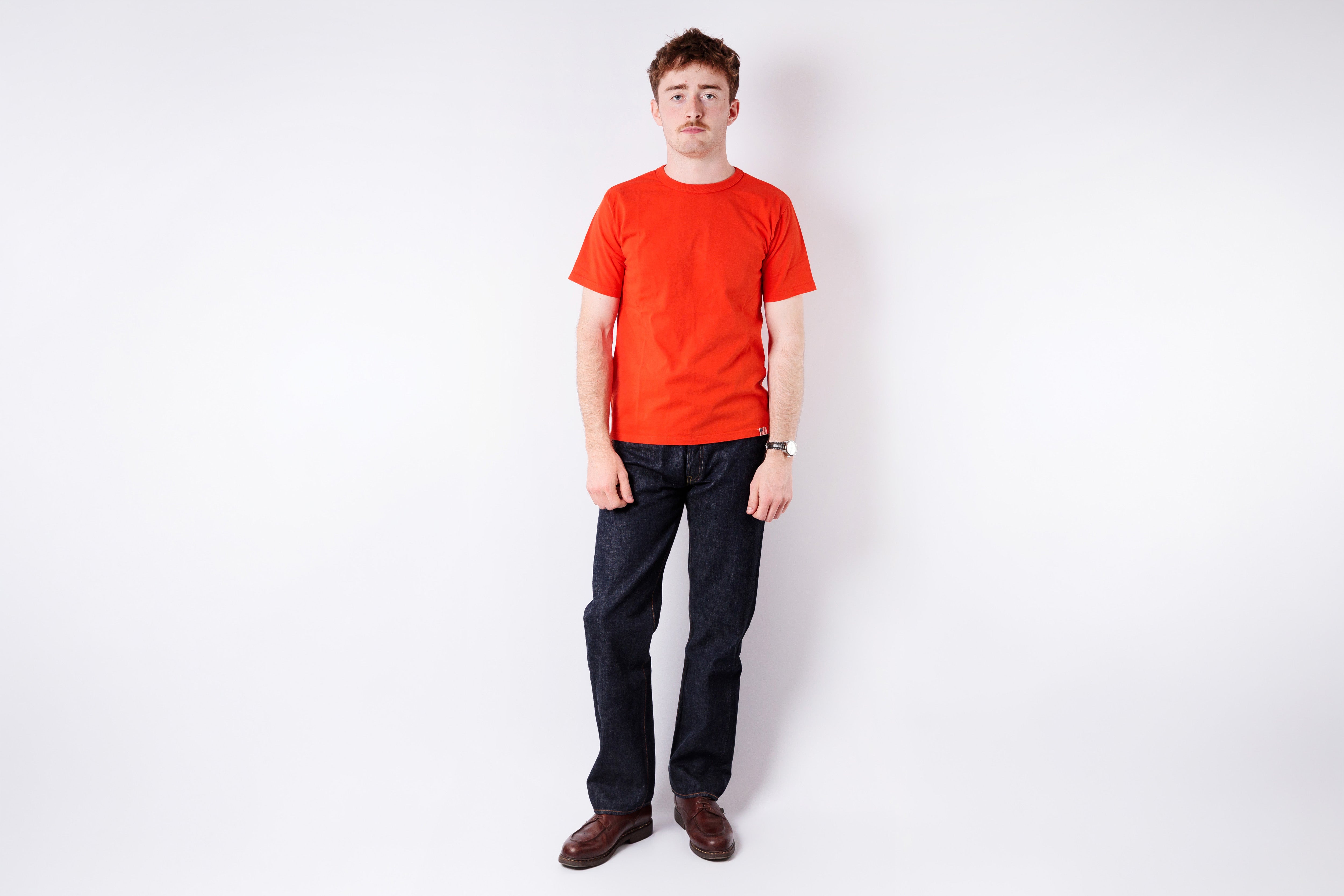 Person wearing a red t-shirt and dark pants on a white background